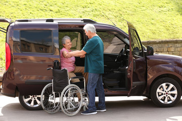 Fototapeta na wymiar Mature man helping senior woman to get out from van into wheelchair outdoors