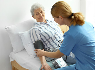 Nurse measuring blood pressure of elderly woman indoors. Medical assistance
