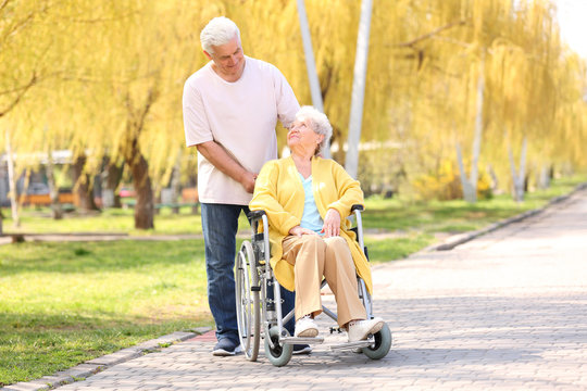 Senior woman in wheelchair and mature man on sunny day outdoors