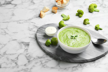 Bowl of broccoli cream soup served on white marble table, space for text