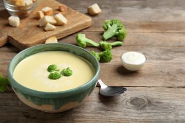 Bowl of cheese cream soup with broccoli served on wooden table, space for text