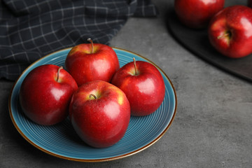 Plate with ripe juicy red apples on grey table