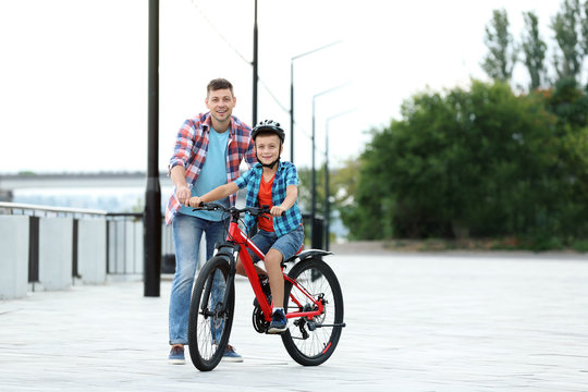 Dad teaching son to ride bicycle outdoors - Powered by Adobe