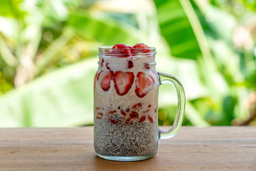 Almond milk chia pudding with fresh red strawberries, goji berries and oat flakes in a glass jar mug. Vegan raw breakfast. Chia seeds and fresh cut fruits and berries dessert