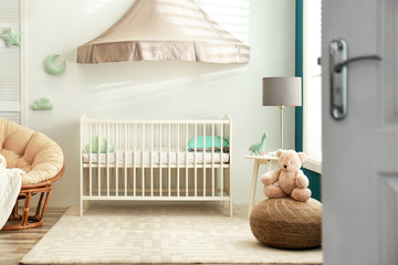 Cute nursery interior with comfortable crib near white wall