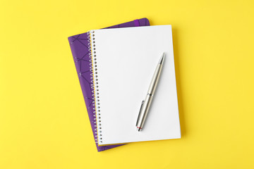 Notebooks and pen on yellow background, top view