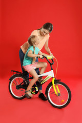 Young mother teaching daughter to ride bicycle on red background