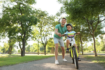 Happy father teaching his son to ride bicycle in park