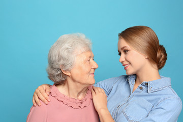 Young woman and her grandmother on light blue background