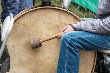 big drum and drummer sitting next to him with a stick outside