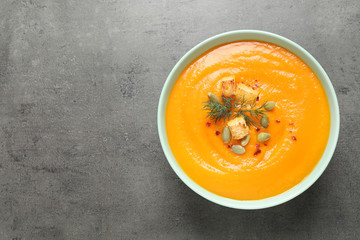 Delicious pumpkin soup in bowl on grey table, top view. Space for text