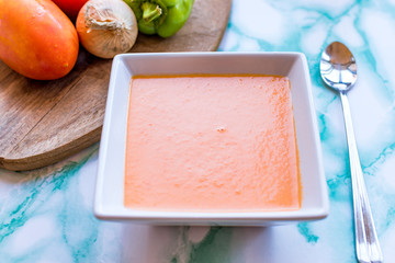 White plate of Andalusian gazpacho with the ingredients aside.