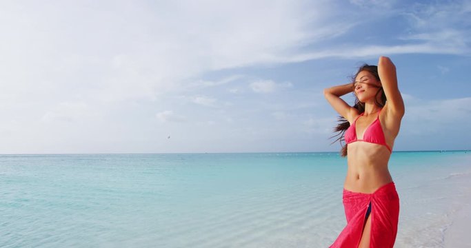 Sexy bikini woman relaxing on beach with slim stomach wearing red bikini top and pareo cover up beachwear - weight loss or epilation concept.