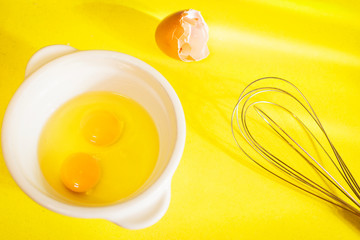 Egg yolks with a whisk on a yellow background