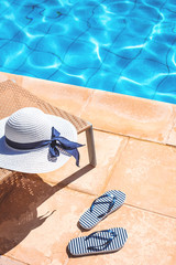 White summer hat with marine flip flops at sunny swimming pool with glowing water in summer. Travel or vacation concept with copy space