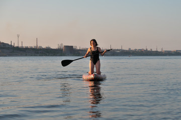 Girl rides on a surfboard with a paddle in sunset light