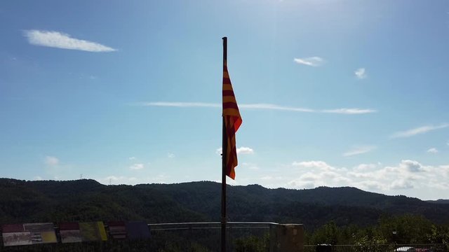 Zoom in on Catalan flag barely moving on top of a hill, overlooking hills with a cloudy sky.