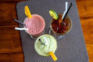 Avocado smoothie, watermelon shake and cold tea in a glass on a wooden table. Tropical drink concept . Top view, closeup