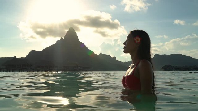 Beach beauty woman natural exotic babe in red swimsuit looking serene at beach sunset Bora Bora, French Polynesia, Tahiti. Asian bikini model body care pampering and natural beuaty concept.