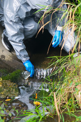 terrorist in a protective suit and gloves, pours liquid from a glass tube with poison, for infection, in reservoirs