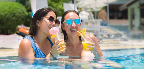 Two women drinking cocktails in a pool, on a summer vacation.