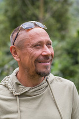 People and lifestyle concept. Happy middle-aged unshaven man outdoor against green nature background. Adult man portrait closeup