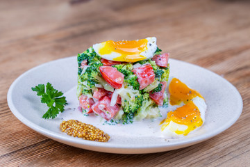 Delicious salad with broccoli, tomato, onion and boiled egg with cream sauce in plate on wooden background. Healthy food