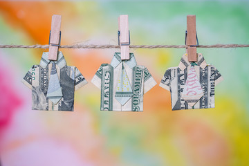 Origami shirt made of dollar banknote on hanging colorful background. Dollar bills hanging on a rope. Close up