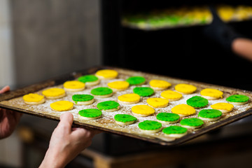 the pastry chef puts in the oven baking sheet with round green and yellow raw eclairs.