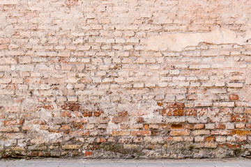 Old weathered vintage brick wall with broken plaster and pavement on the ground. Grungy urban...