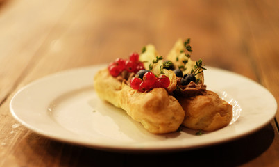 eclairs decorated with fresh berries on a white plate, handmade, culinary theme, close up