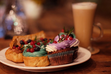 cupcake and eclairs on a plate next to latte coffee, warm colors, delicious desserts, close up