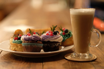 cupcake and eclairs on a plate next to latte coffee, warm colors, delicious desserts, close up