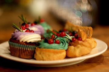 cupcake and eclairs on a plate next to latte coffee, warm colors, delicious desserts, close up