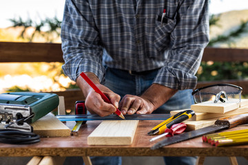 Adult craftsman carpenter with pencil and ruler tracing the cutting line on a wooden table. Housework do it yourself. Stock photography.