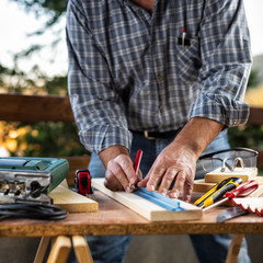 Adult craftsman carpenter with pencil and ruler tracing the cutting line on a wooden table. Housework do it yourself. Stock photography.