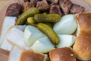 Set of delicious ukrainian food, close up. Cucumber, onion, fat, bun and sausage on a plate