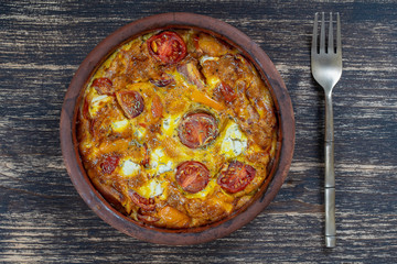 Ceramic bowl with vegetable frittata, simple vegetarian food. Frittata with tomato, pepper, onion and feta cheese on wooden table, close up. Italian egg omelette