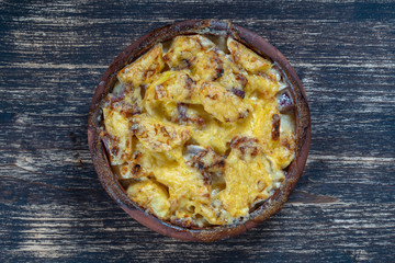 Baked potato, onion and garlic with cheese on the wooden table, close up. Ceramic bowl with potato onion and garlic slices background
