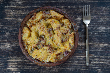 Baked potato, onion and garlic with cheese on the wooden table, close up. Ceramic bowl with potato onion and garlic slices background