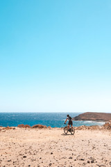 Fototapeta na wymiar person on mountain bike bicycle in desert landscape near coast with ocean background