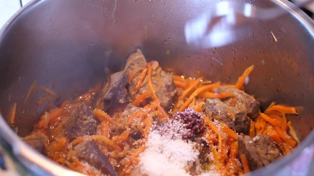 Adding spices to meat crots and carrots when cooking Plov traditional dish from Uzbekistan