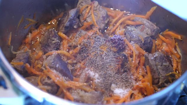 Adding spices to meat crots and carrots when cooking Plov traditional dish from Uzbekistan
