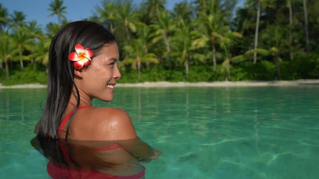 Beach beauty woman Natural exotic babe in red swimsuit looking serene on tropical beach. Asian bikini model wearing hibicus flower for body care pampering.