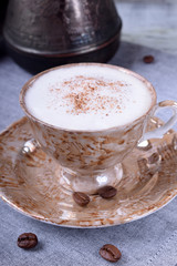 Freshly brewed coffee with a milky foam topped with cinnamon in a brown cup