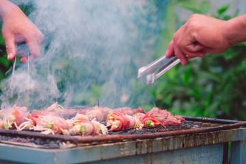 Bacon roll with enoki mushroom grilled. The bacon wrapped in needle mushroom being roasted with charcoal on the grill. Barbecue grilled mushrooms on steel grill on charcoal stove burned and smoke 