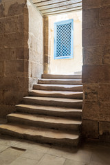 Old narrow dark passage and staircase leading to outdoor small lobby with blue wooden windows
