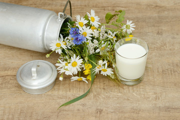 glass milk and wild flowers in the milk churn on wooden table