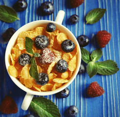 Healthy eating, food and diet concept - Cornflakes with berries raspberries and blueberries on blue wooden background. Top view.