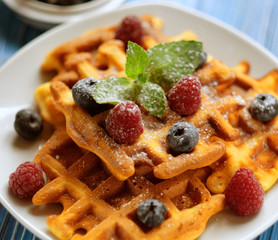 Traditional belgian waffles with fresh berrys and sugar powder on white plate, blue wooden background. Flat lay, top view, copy space.